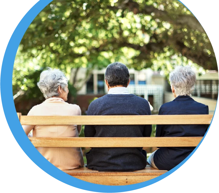 Drei Senioren sitzen gemeinsam auf einer Holzbank im Grünen und genießen die Natur – Gemeinschaft erleben in den Reinery Wohngemeinschaften.