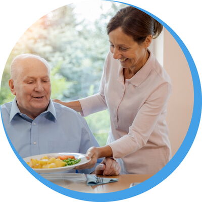 Eine freundliche Mitarbeiterin serviert einem Senior ein frisches Menü – der zuverlässige Menüservice „Essen auf Rädern“ von Reinery.