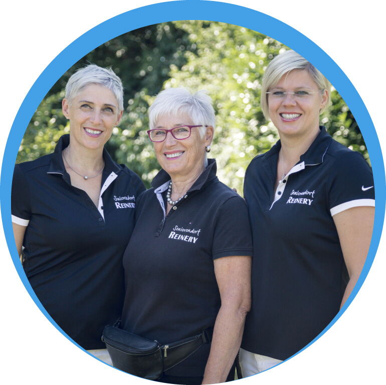 Drei lächelnde Mitarbeiterinnen der Reinery Pflege GmbH in einheitlicher Dienstkleidung vor natürlichem Hintergrund.